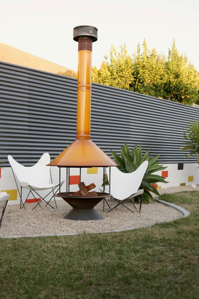mid century backyard with vintage butterfly chairs fireplace and corrugated fence